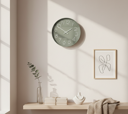 Green wall clock on a beige wall with a shelf below featuring books, a vase, and a towel.