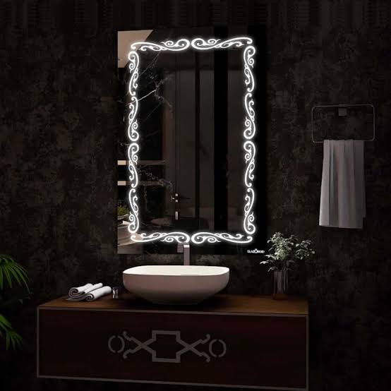 Bathroom vanity with illuminated decorative mirror on a dark wall.